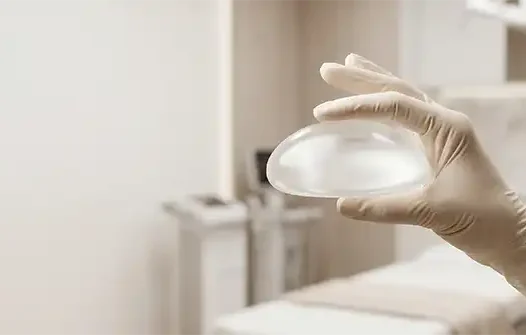 Seguridad en Mamoplastia de Aumento Mano con guante quirúrgico sosteniendo un implante para mamoplastia de aumento segura con el Dr. Minyor Avellaneda.