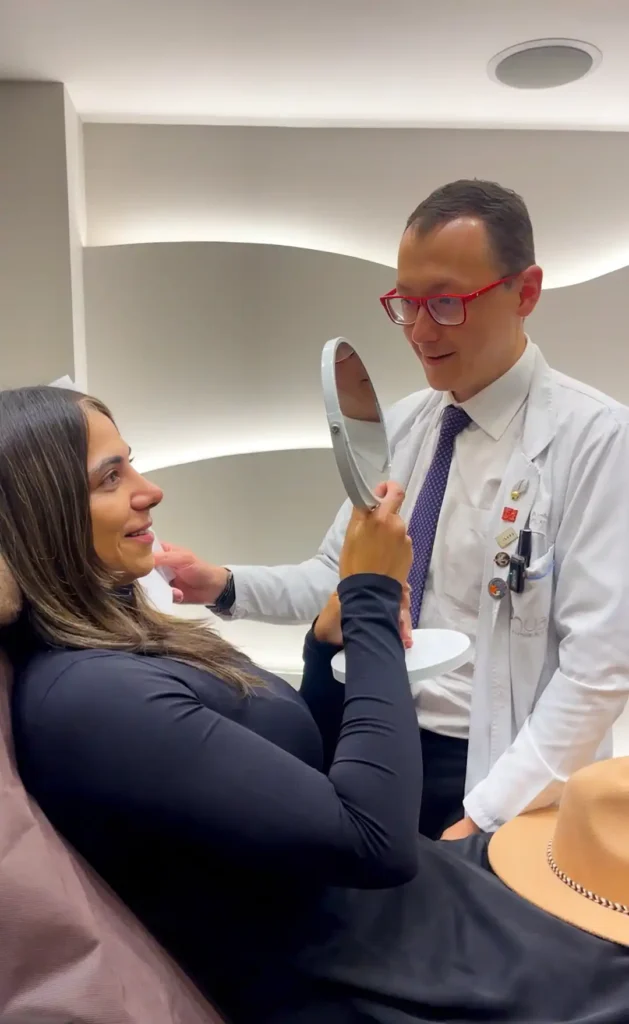 Paciente en consulta de recuperación de rinoplastia con el Dr. Minyor Avellaneda viendo sus resultados en un espejo.